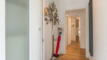 Un couloir doté d’un plancher en bois, un porte-manteau sur lequel sont accrochés divers objets, et une porte donnant sur une autre pièce.