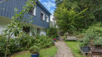 Een pad dat leidt naar een huis met een blauwe gevel, omringd door weelderig groen en een houten bankje.