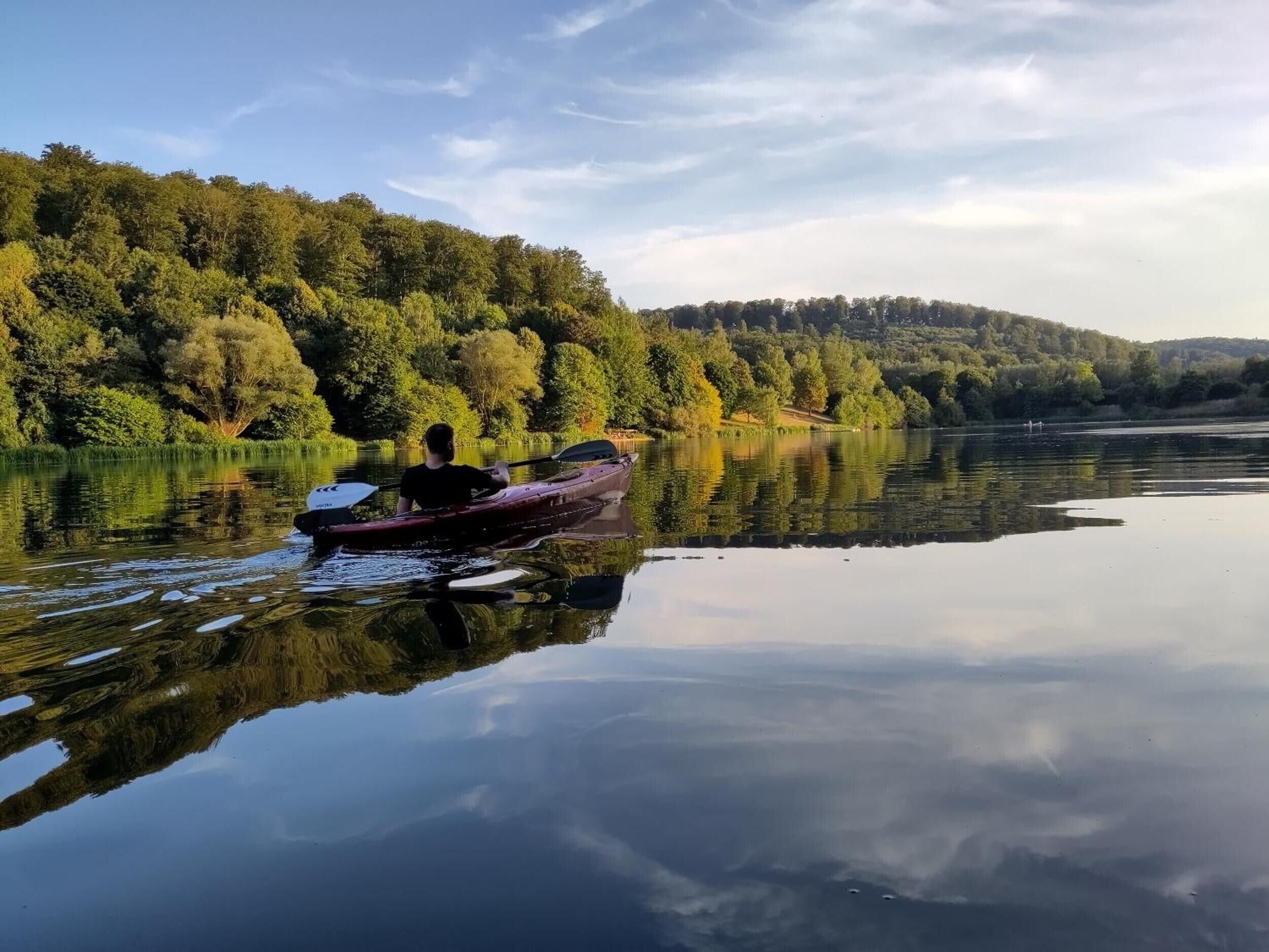 Ein ruhiger See mit einem einzigen Boot, das an der Küste vor Anker liegt, umgeben von dichtem Wald.