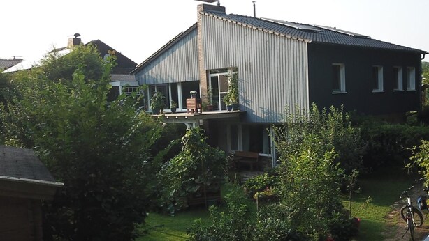 Un immeuble d’habitation doté d’un balcon, entouré de verdure et avec un vélo à proximité.
