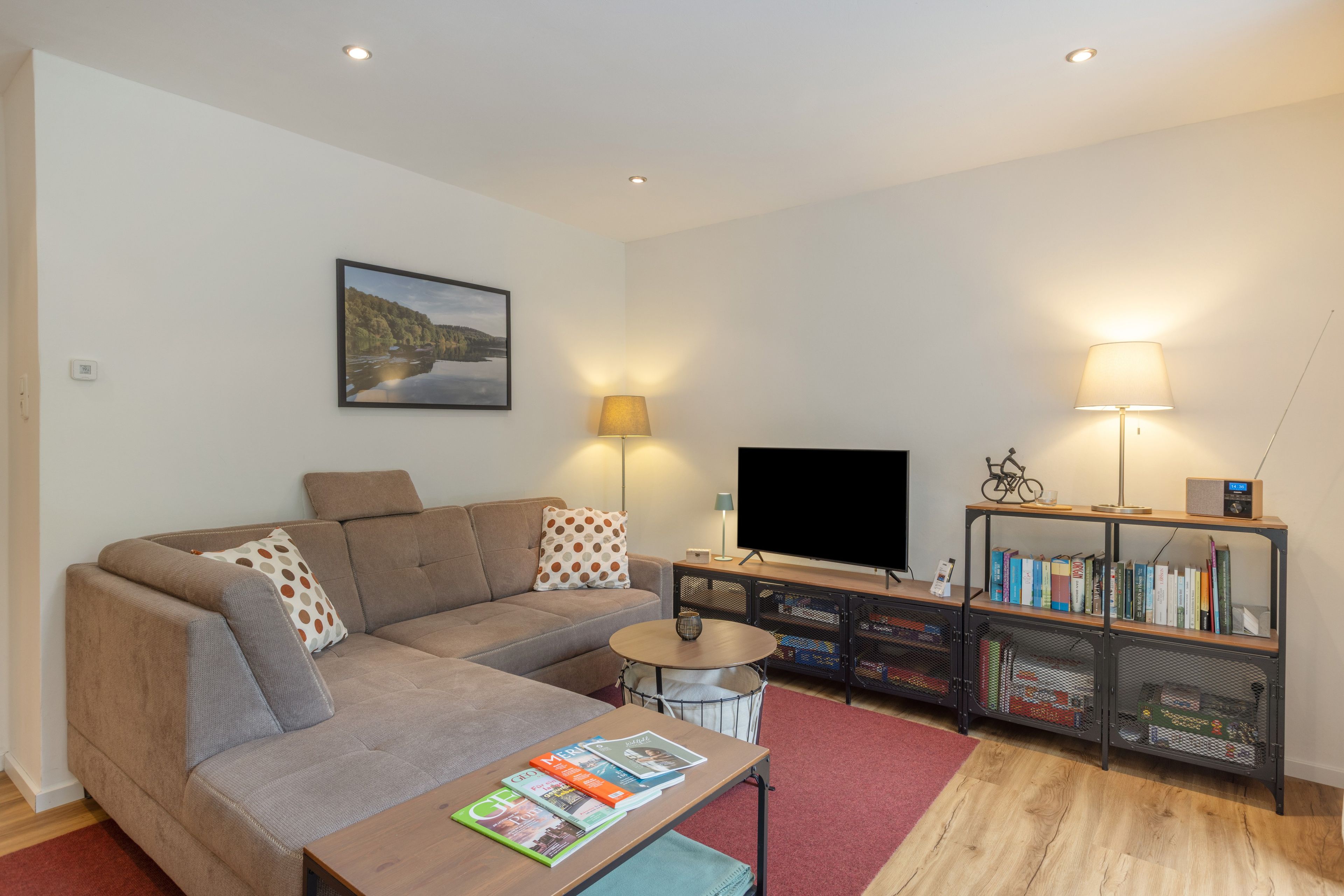 Ein modernes Wohnzimmer mit Sofa, Couchtisch, Flachbildfernseher, Bücherregal und einem Gemälde an der Wand.