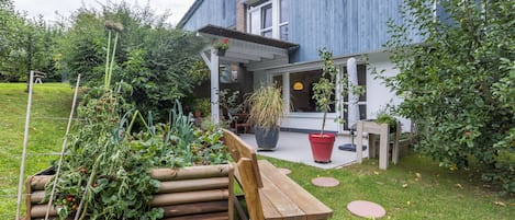 Un edificio moderno blu con una terrazza in legno, piante in vaso e una panchina in legno.