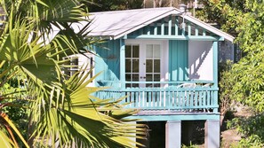 A small, single-story building with a balcony, surrounded by lush greenery.