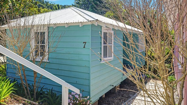 A small, single-story building with a light blue exterior, a white door, and a window with a white frame. - Sage by Hyams Beach Seaside Cottages | Romantic, iconic heritage cottage (Hyams Beach)