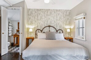 Un dormitorio con una cama grande, dos mesitas de noche, una lámpara de pared y una ventana con contraventanas.