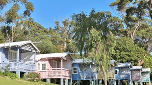 A row of traditional wooden houses with verandas, surrounded by lush greenery. - Sage by Hyams Beach Seaside Cottages | Romantic, iconic heritage cottage (Hyams Beach)