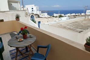 A balcony with a table and chairs, potted plants, and a view of the sea and white buildings. - Akrotiri Flat near Red Beach (akrotiri)
