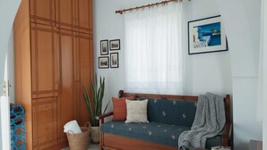 Ein gemütliches Wohnzimmer mit einem Holzschrank, einer gepolsterten Couch mit gemusterten Kissen, einem Topf mit Pflanze und einem gerahmten Bild an der Wand.