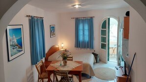 Ein Schlafzimmer mit Bett, Schreibtisch und Stuhl. Es gibt ein Fenster mit Vorhängen, eine Tür zu einem anderen Raum und ein Bild an der Wand.