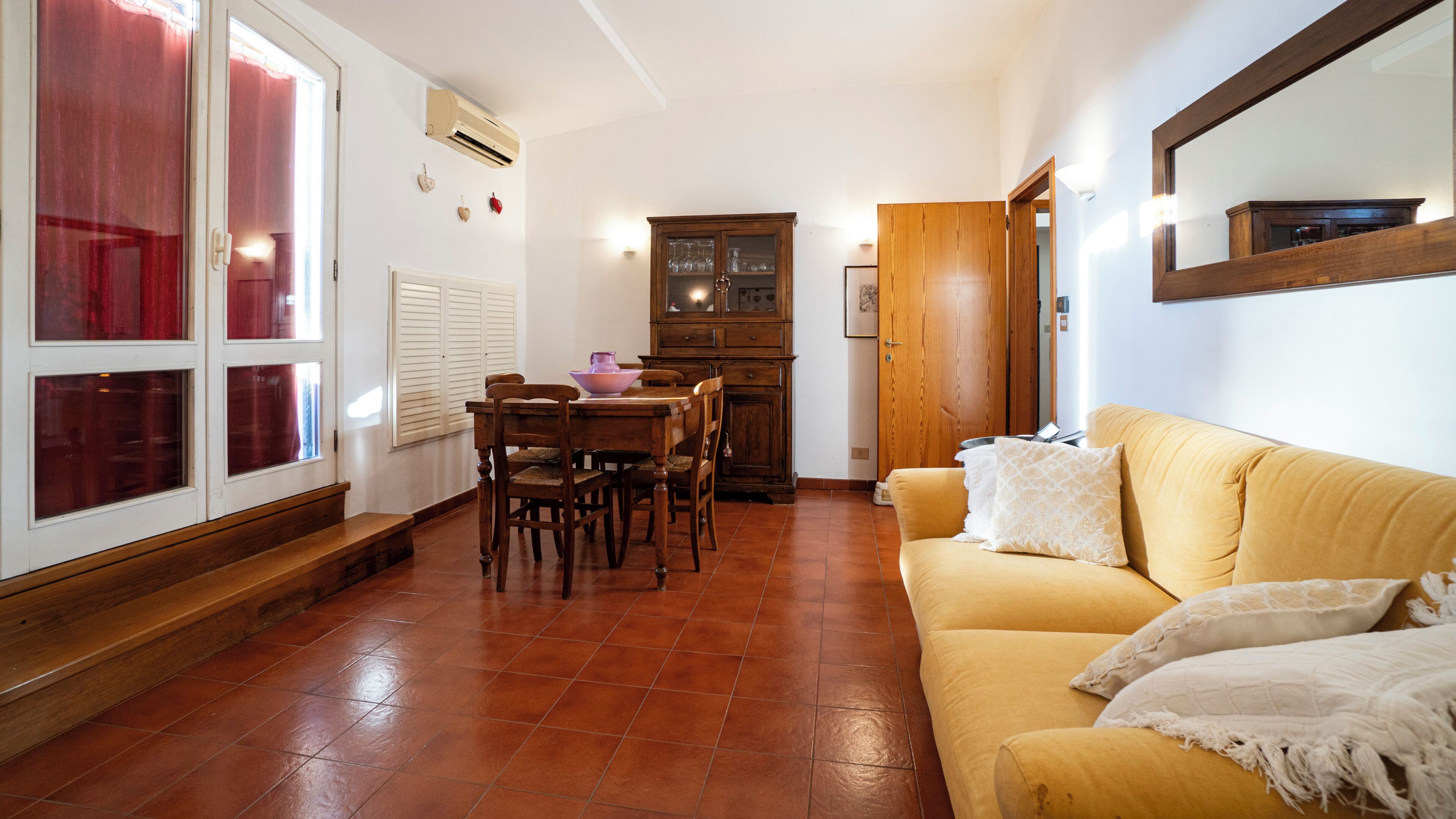 Una sala de estar con un sofá amarillo, una mesa de comedor de madera y sillas.