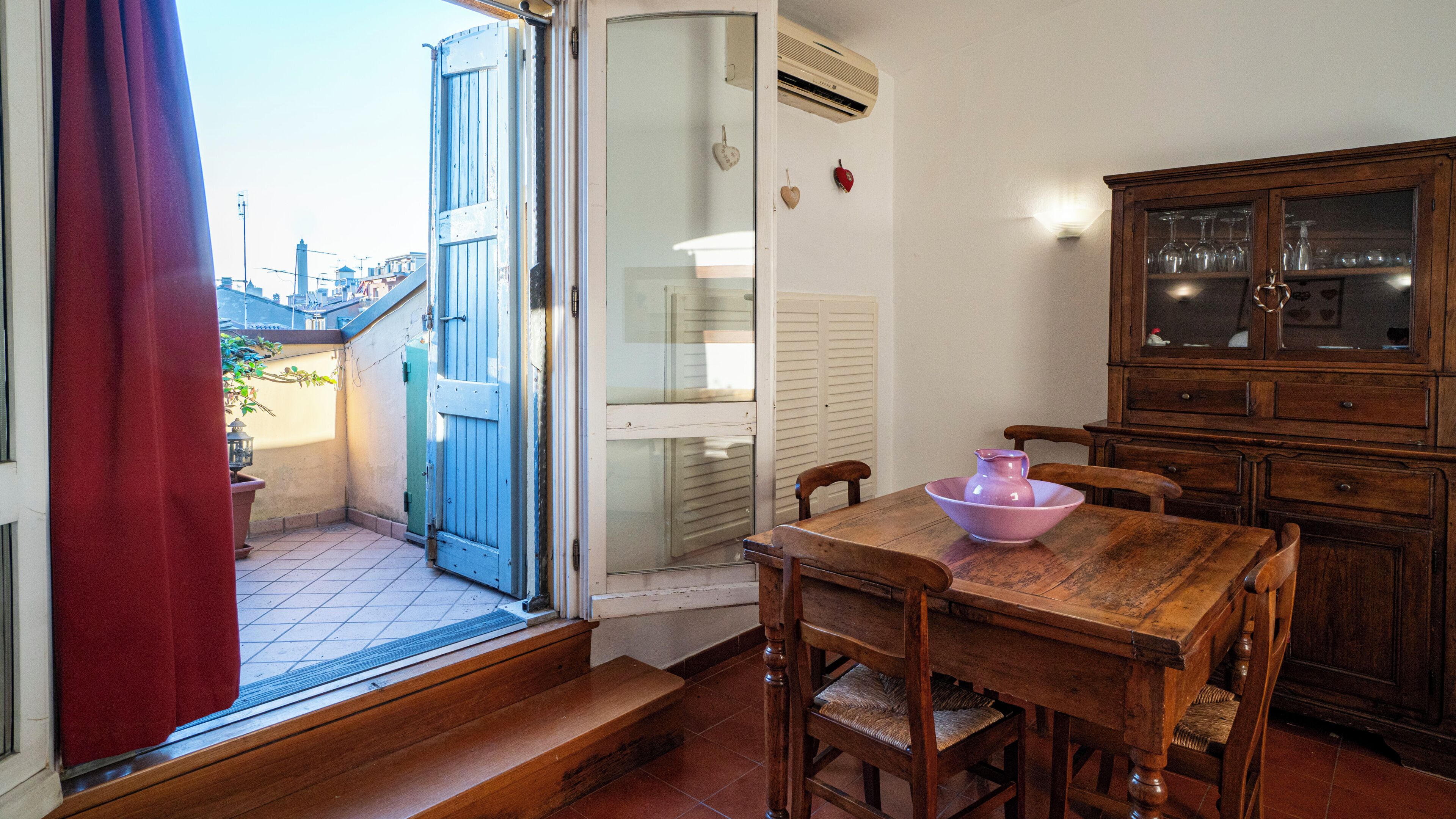 Un comedor con una mesa de madera, sillas, un armario con puertas de vidrio y un ventanal corredero que da a un espacio exterior.