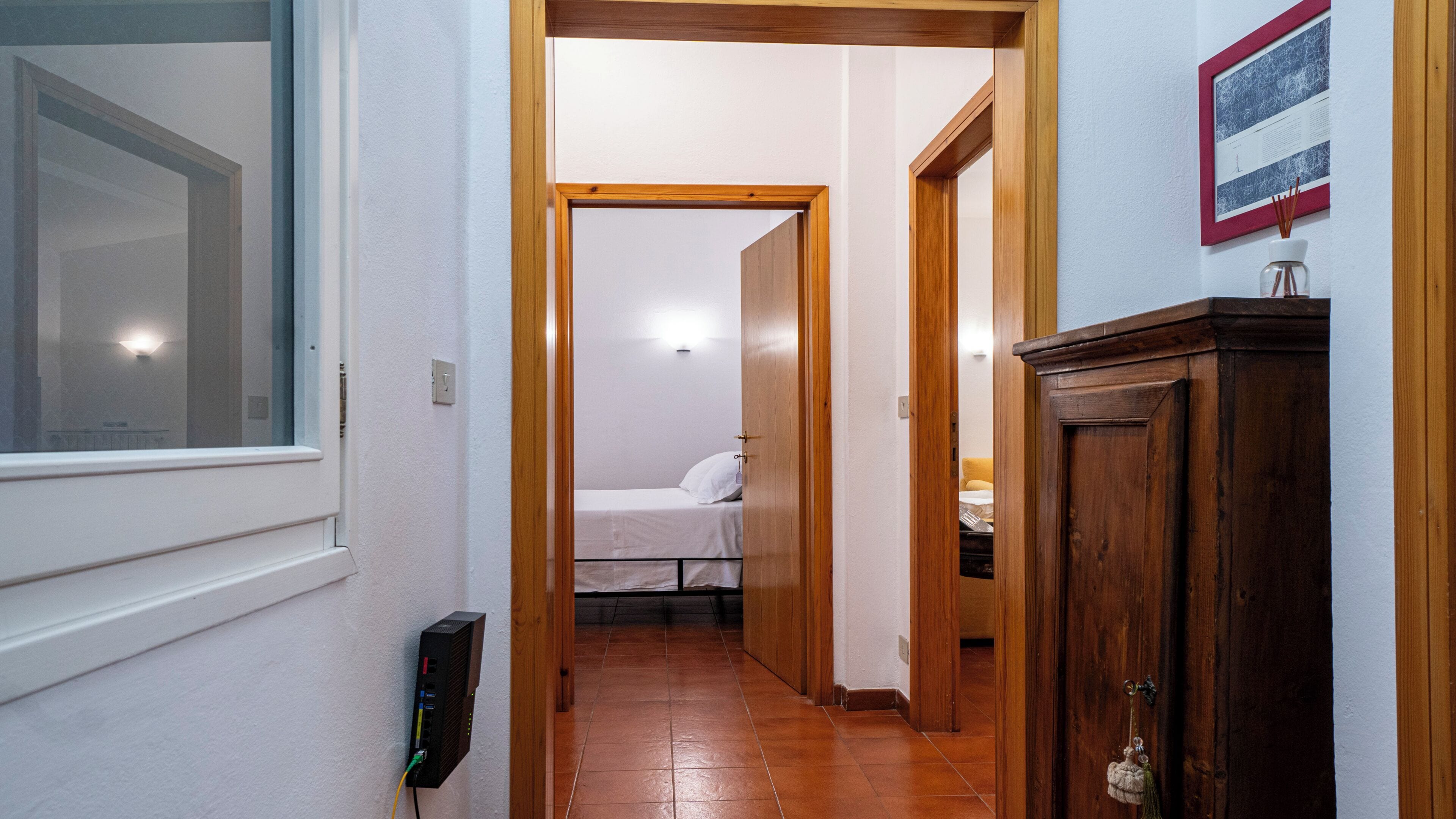 A hallway leading to a bedroom with a bed, a wooden cabinet, and a framed picture on the wall.