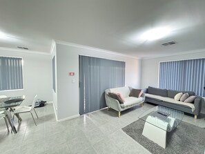 A modern living room with a glass coffee table, two sofas, a dining table with chairs, and a sliding door.