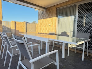 An outdoor patio with a glass-top table and white metal chairs.