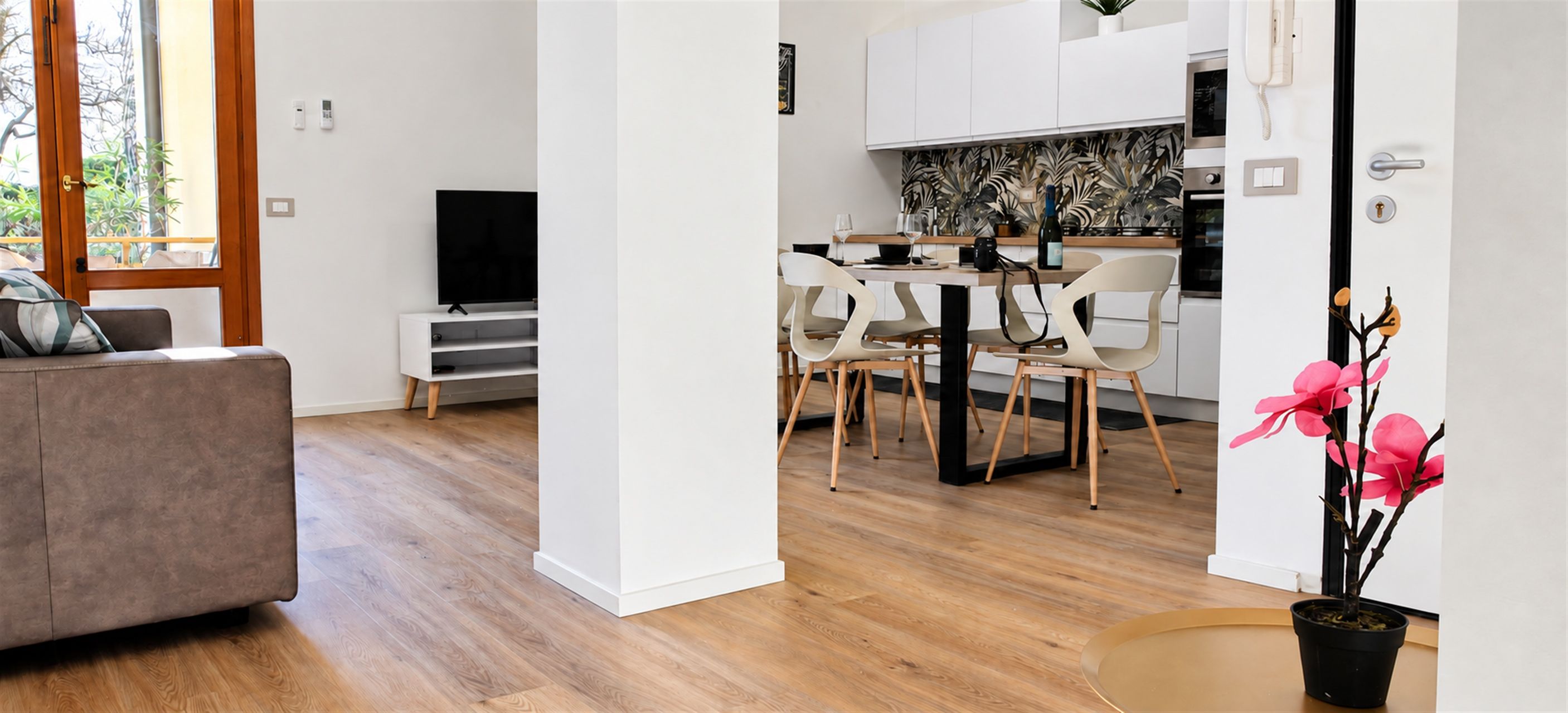 A modern living room with a sofa, a television, and a dining area with chairs and a table.