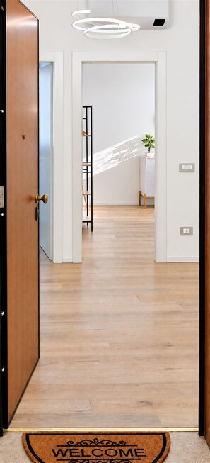Ein Flur mit Holzboden, Fußmatte, einer modernen Lampe und einer Tür.