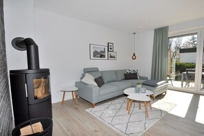 Ein modernes Wohnzimmer mit einem schwarzen Kaminofen, einem grauen Sofa und einer Glastür, die auf einen Balkon führt.