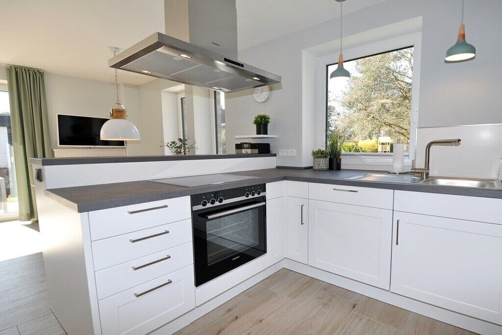 Une cuisine moderne avec des meubles blancs, un four encastré et des luminaires suspendus.
