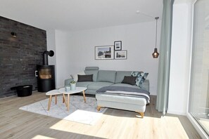 A modern living room with a sofa, a small table, a fireplace, and a large window. - Holiday home with 2 bedrooms (St.Peter-Ording)