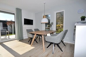 Ein moderner Essbereich mit einem Holztisch, grauen Polsterstühlen, einer Pendelleuchte und Blick durch eine Glastür.