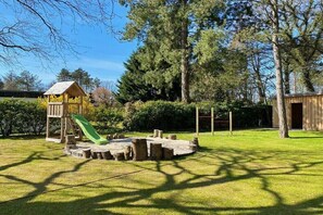 Ein Spielplatz mit Rutsche und Klettergerüsten, umgeben von einer Rasenfläche und Bäumen.