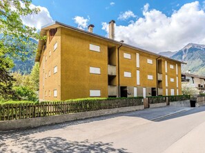 A multi-story building with a yellow facade, balconies, and a view of mountains. - Cosy apartment for 4 people with TV and patio (Giustino)