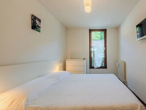Une chambre avec un lit, une fenêtre, un radiateur et un téléviseur fixé au mur.