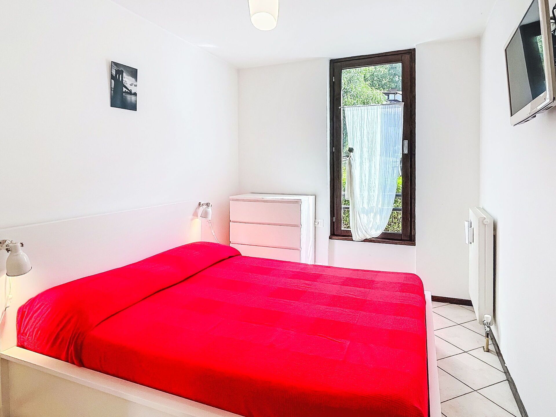 Une chambre à coucher avec un lit, une commode, une fenêtre et un téléviseur.