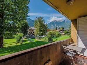 Ein Balkon mit Blick auf einen grünen Park, ein Gebirge und Wohnhäuser.