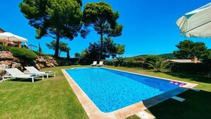 Una piscina rectangular amb una superfície d'aigua blava cristal·lina, envoltada d'un jardí ben cuidat i unes quantes gandules.