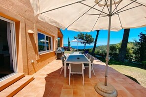Una terrazza esterna con tavolo e sedie, un ombrellone grande e vista sul mare.