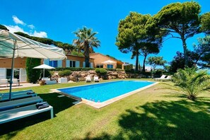 Ein Swimmingpool mit Liegestühlen und Sonnenschirmen, umgeben von einer gepflegten Rasenfläche und Bäumen.