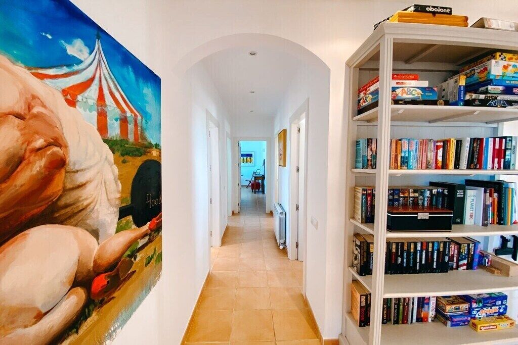 Un couloir avec une bibliothèque remplie de livres et de jeux, et un tableau accroché au mur.