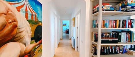 Un couloir avec une bibliothèque remplie de livres et de jeux, et un tableau accroché au mur.