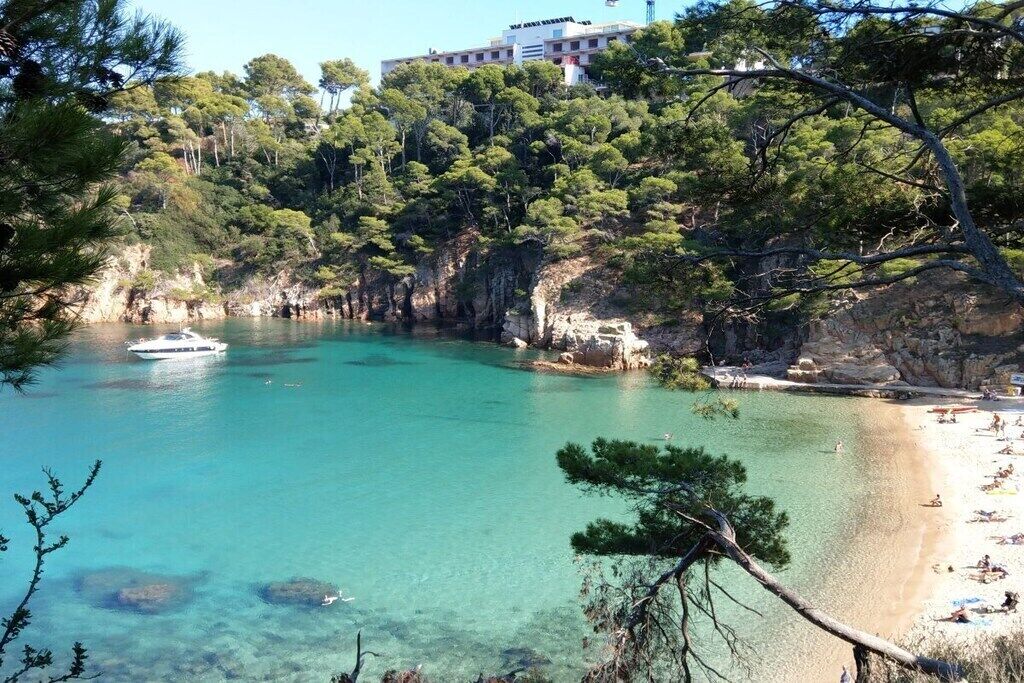 Une zone côtière avec une eau turquoise et limpide, une plage de sable et un bâtiment visible au loin.