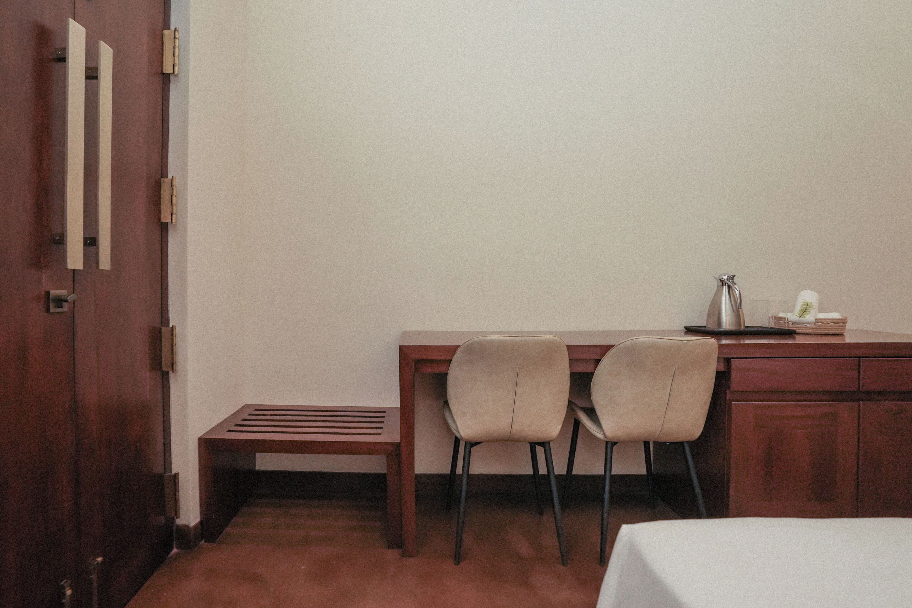Habitación de hotel con un escritorio de madera, dos sillas, una mesita con hervidor y una cama.
