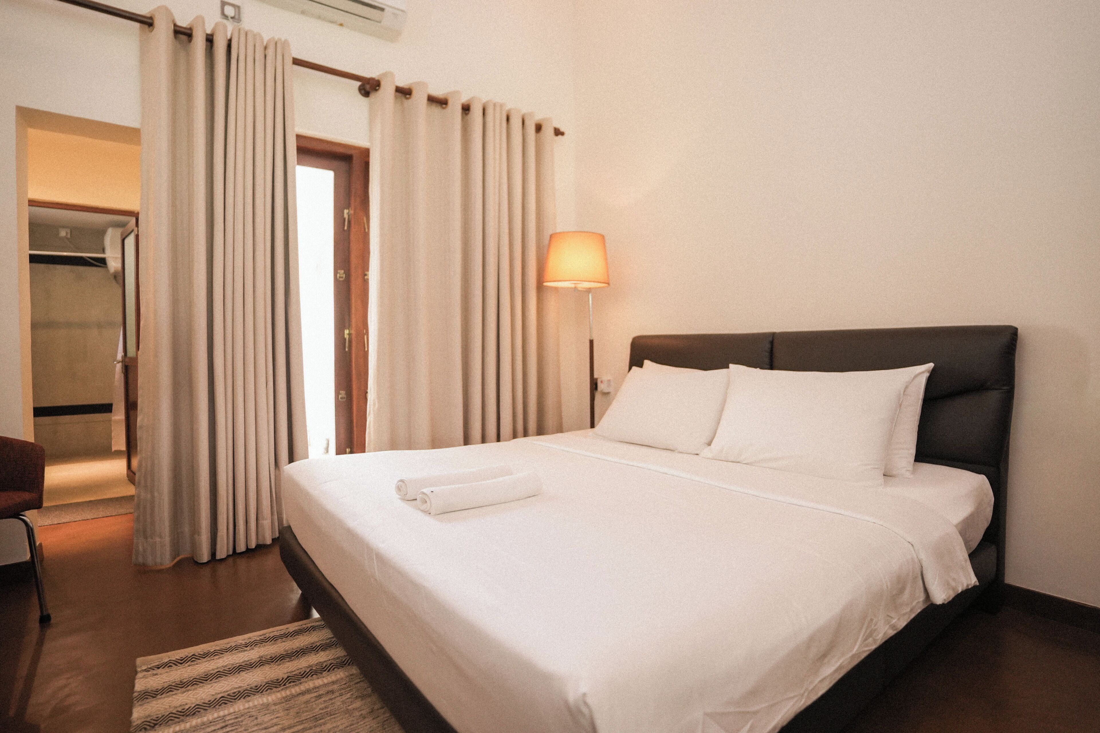 Una habitación de hotel con cama, cortinas, lámpara y una silla.