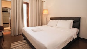 Et hotelværelse med seng, gardiner, en lampe og en stol.