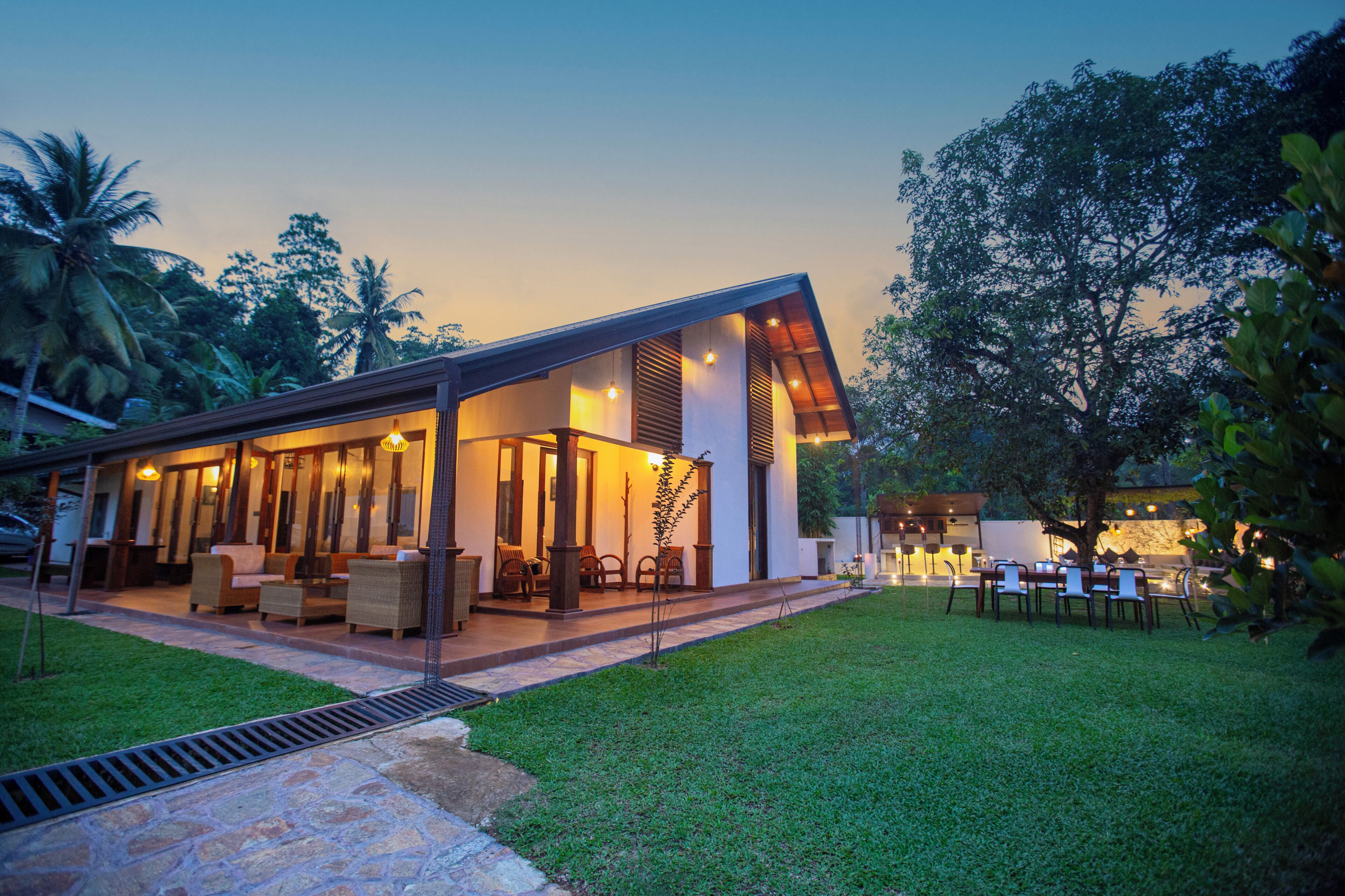 Una casa moderna con un patio cubierto, mobiliario exterior y un césped bien cuidado.