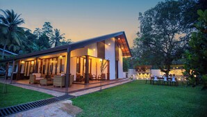 A modern house with a covered patio area, outdoor seating, and a well-maintained lawn.