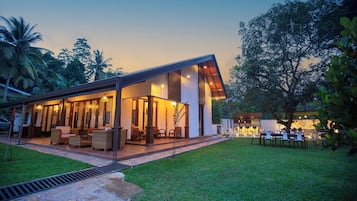 Una casa moderna con un patio cubierto, mobiliario exterior y un césped bien cuidado.