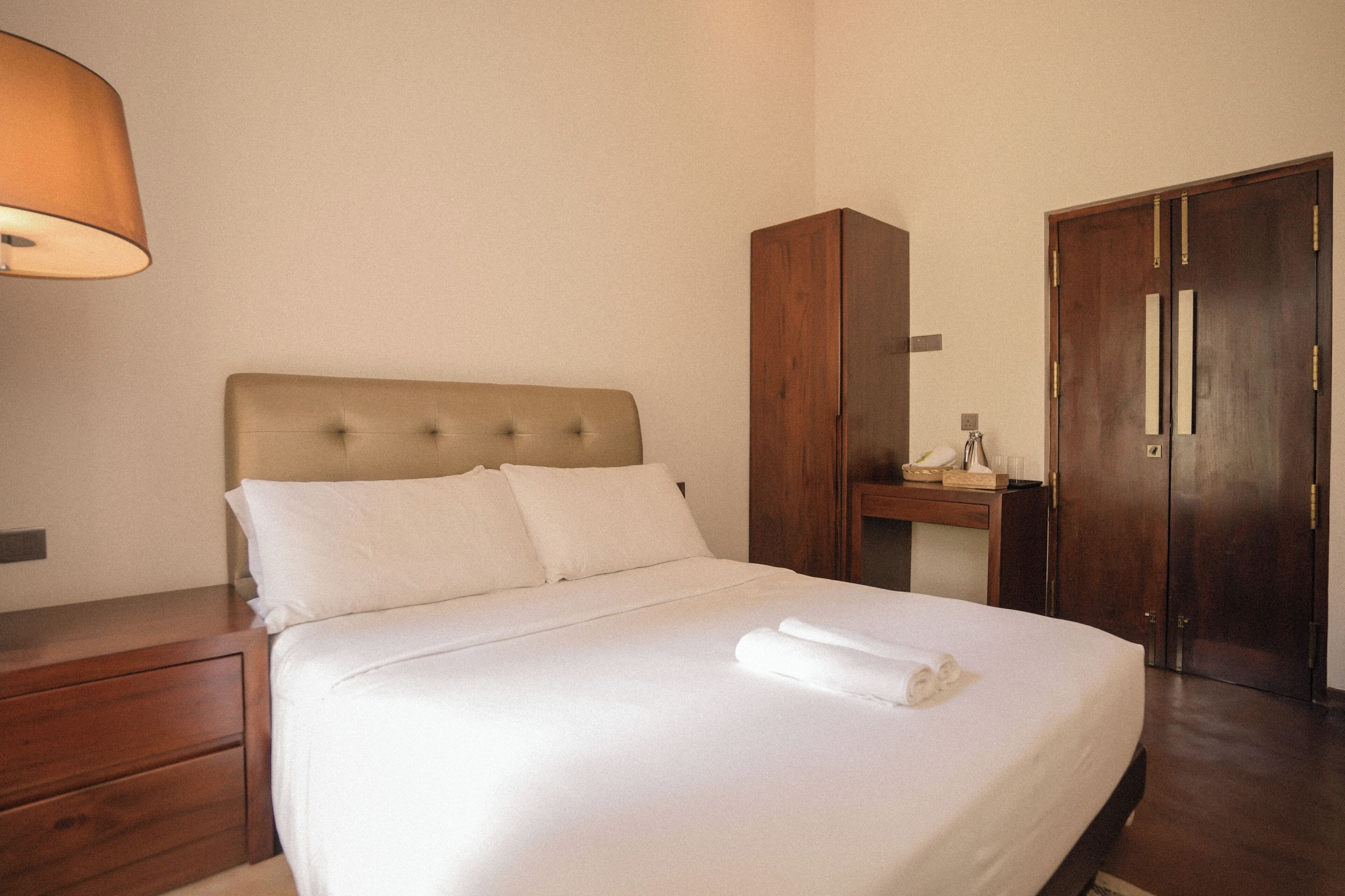 Une chambre d’hôtel comprenant un lit, une table de chevet, une armoire et un bureau avec une lampe.