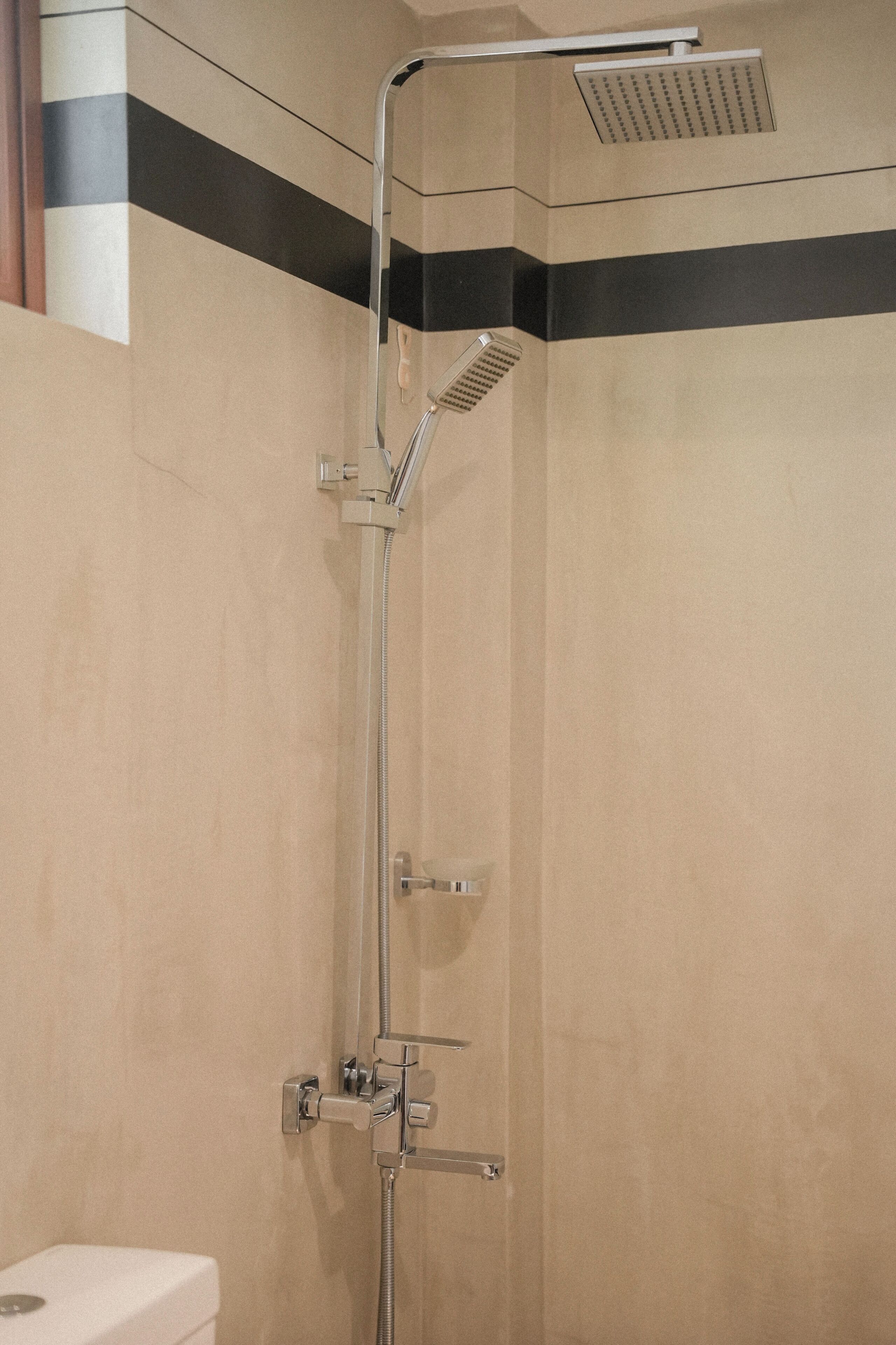 A shower with a handheld showerhead and a wall-mounted control panel.