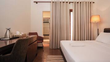 Habitación de hotel con cama, escritorio, silla, lámpara y baño visible a través de una cortina.