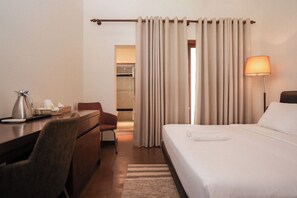 Camera d'albergo con un letto, una scrivania, una sedia, una lampada e un bagno visibile attraverso una tenda.