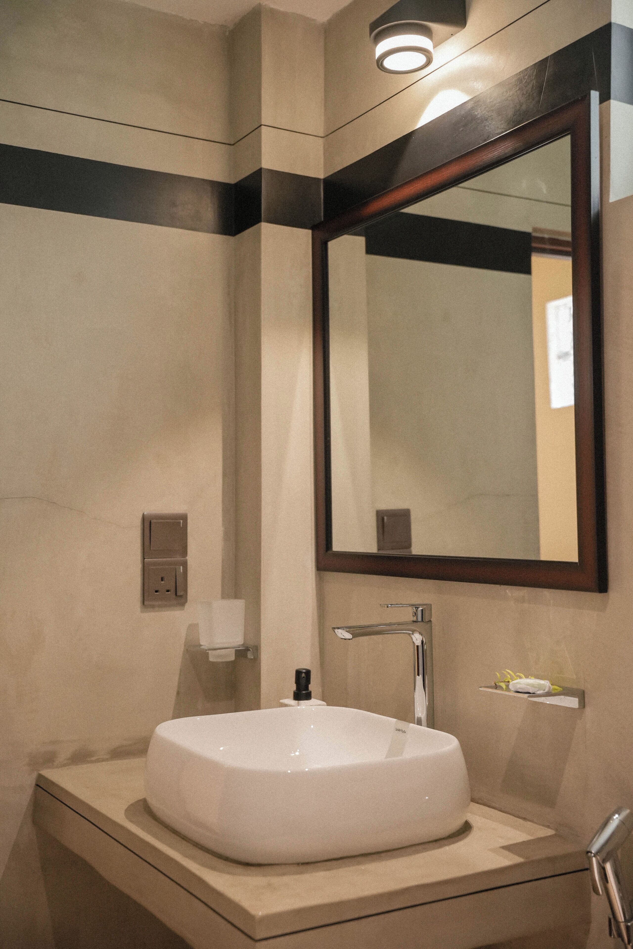 Un baño con lavamanos blanco, espejo y dispensador de toallas.
