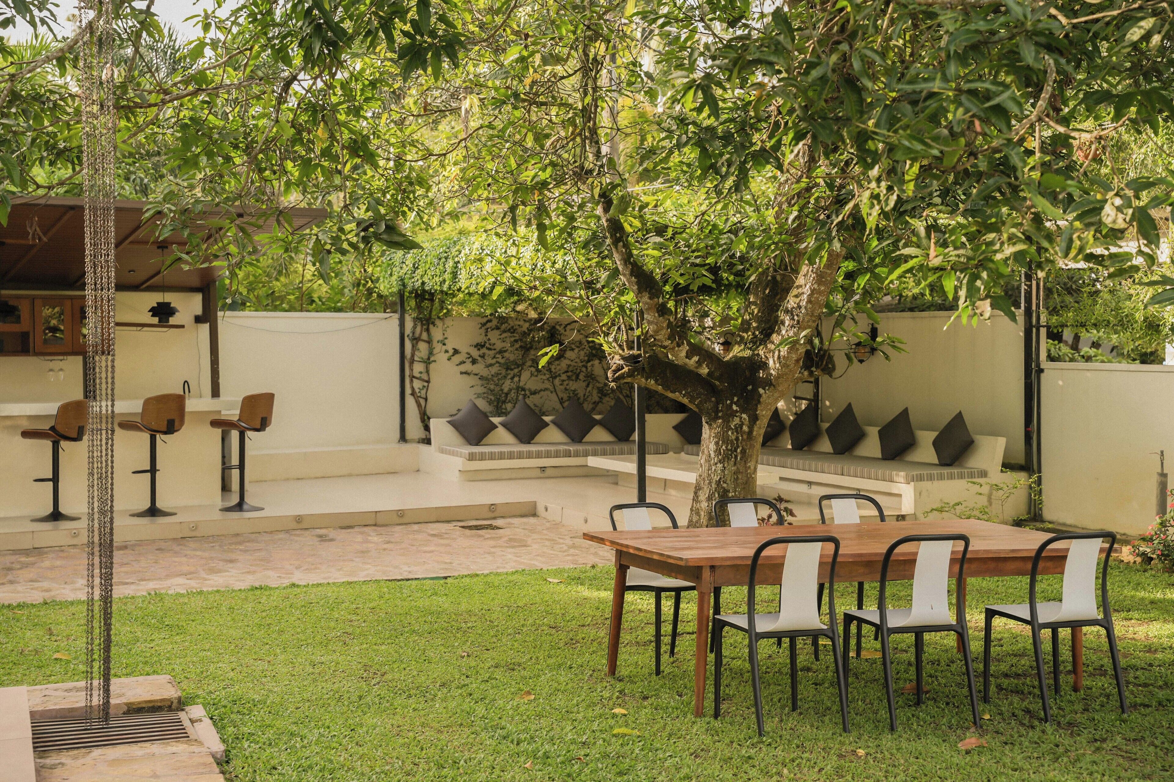 Un área de estar al aire libre con una mesa y sillas, rodeada de follaje y un árbol.