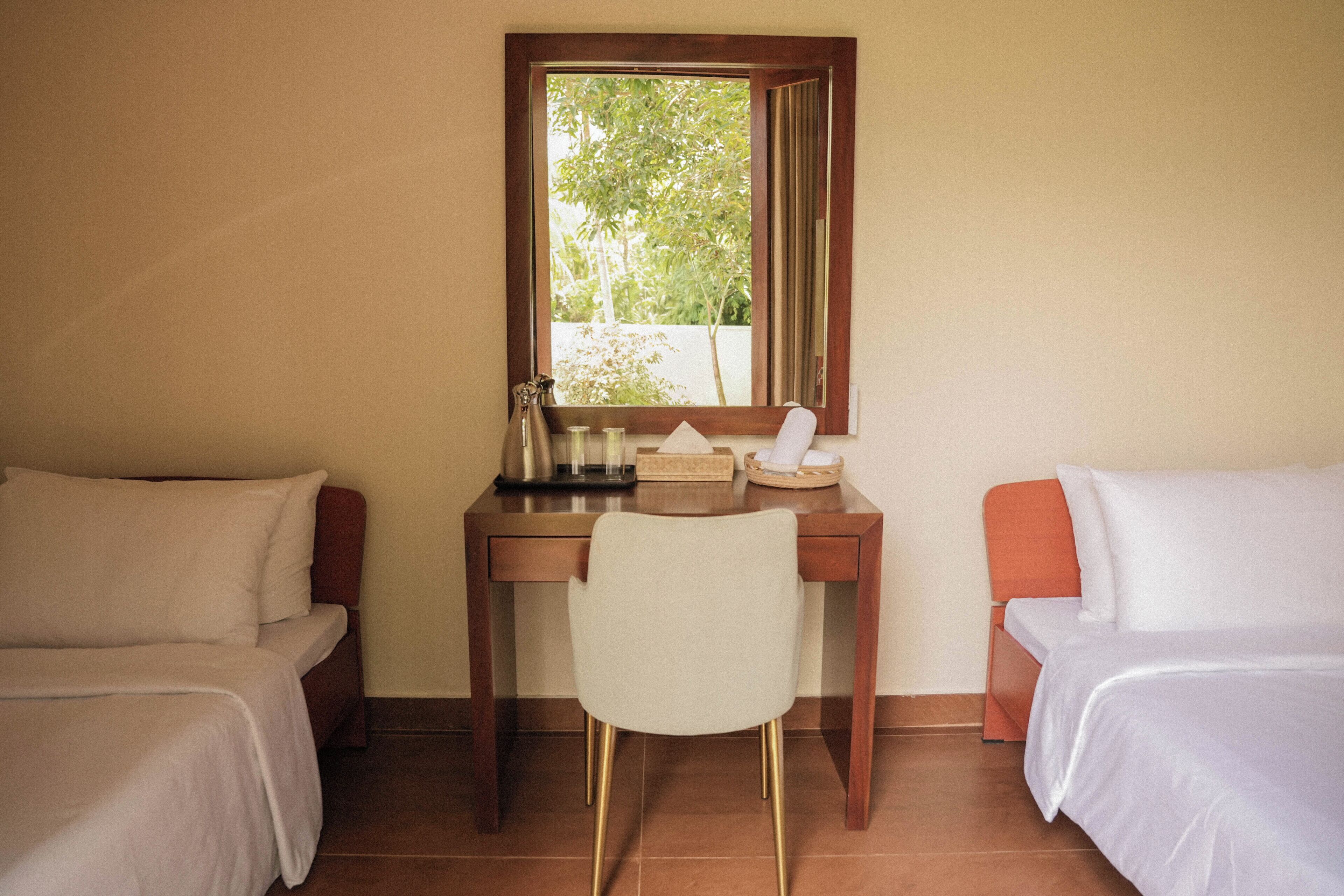 Habitación de hotel con una cama individual, un escritorio con silla, un espejo y una ventana con vista a follaje.