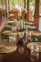 Una larga mesa de comedor con individuales tejidos, un florero central y cristalería.
