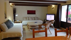 Quarto de hotel com duas camas, televisão, mesa pequena e cadeira de vime.